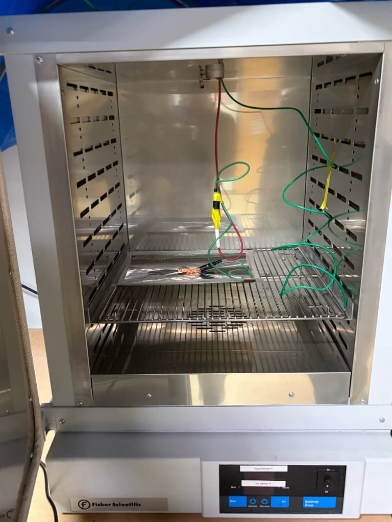 Piezoelectric sample mounted inside a Fisher Scientific Isotemp oven with wired probes and alligator clips