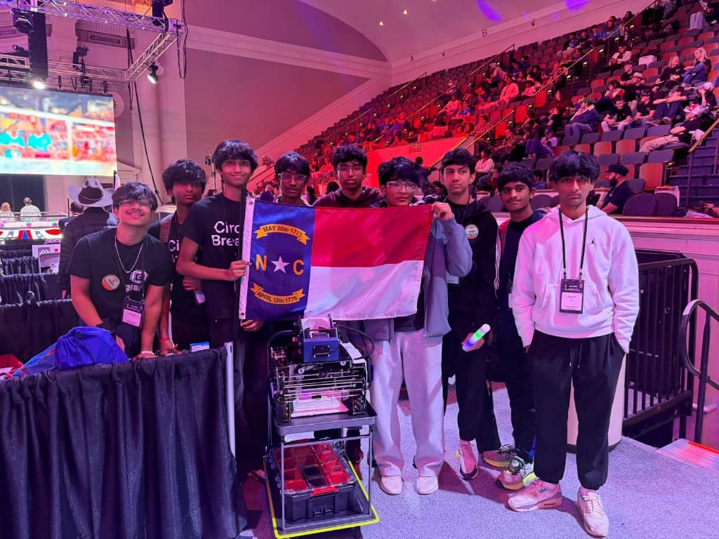 Circuit Breakers team members holding the North Carolina flag at an FTC competition with a 3D printer on a rolling cart