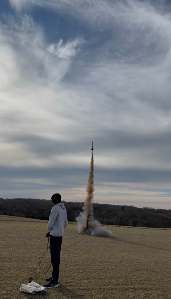 Model rocket ascending with a smoke trail from a field launch, operated via remote controller