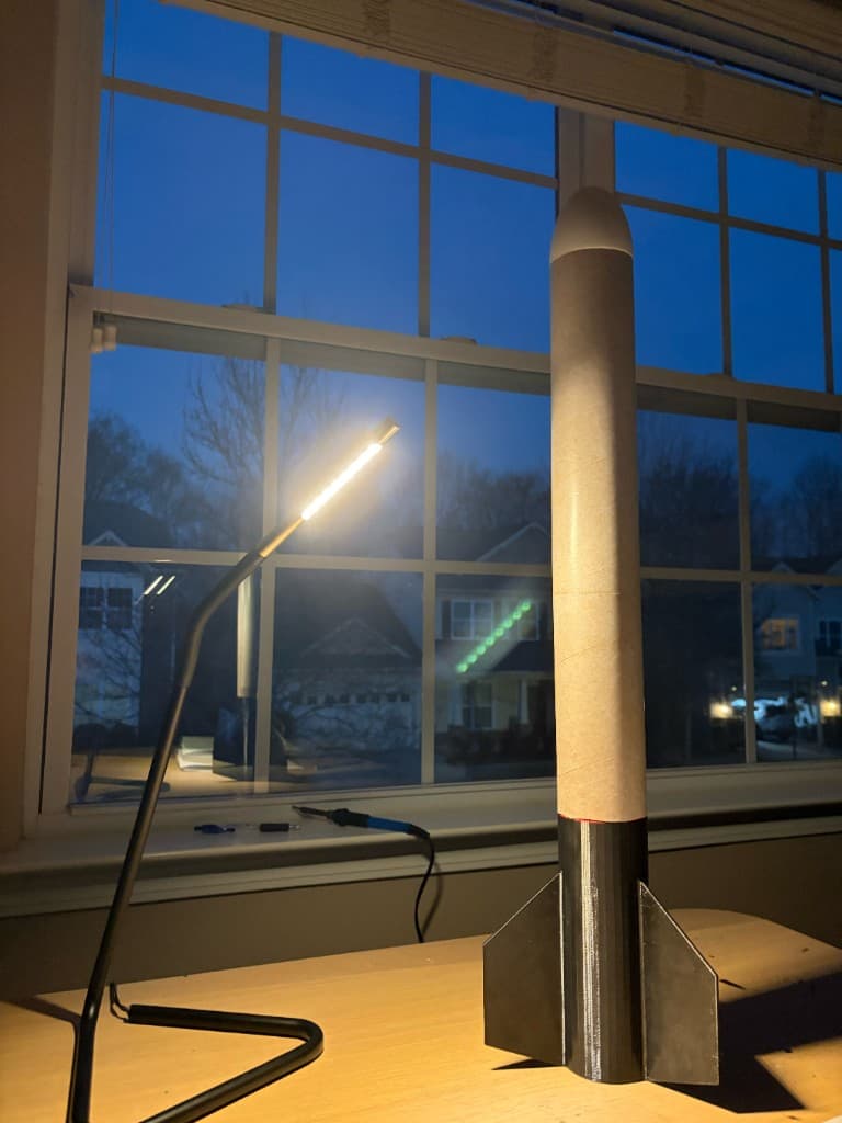 Model rocket with 3D-printed fin assembly on a desk in a home workshop