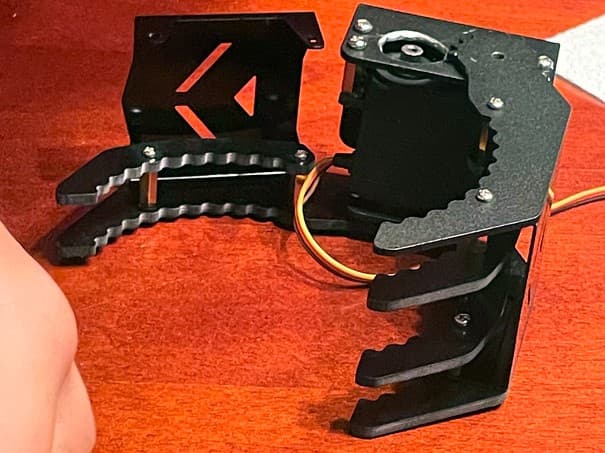 Black robotic servo claw with serrated grippers on a wooden table