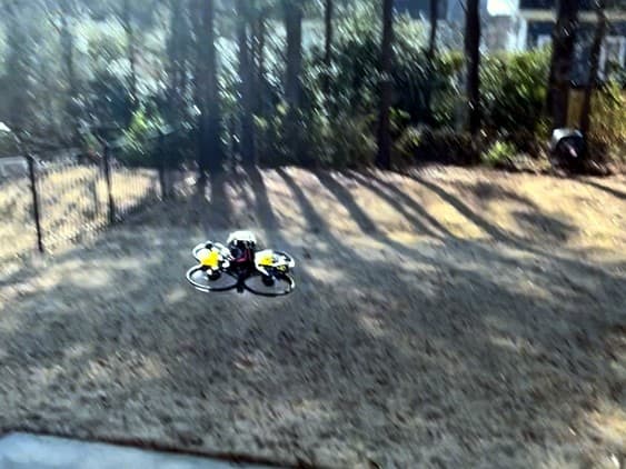 FPV cinewhoop drone hovering over a backyard lawn